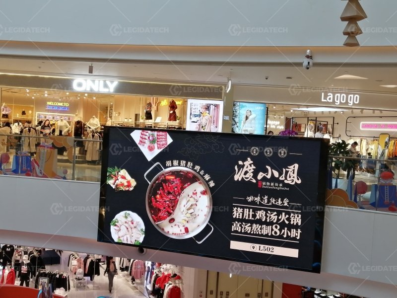 Shoppers walking through a mall concourse with LED display screens on the walls